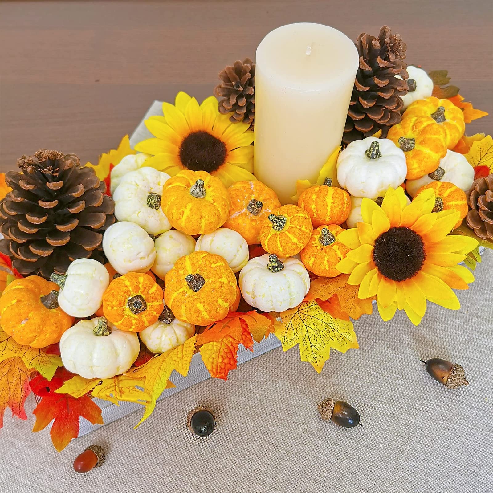 Assorted orange and cream mini pumpkins with sunflowers, pinecones, and autumn leaves arranged around a candle.