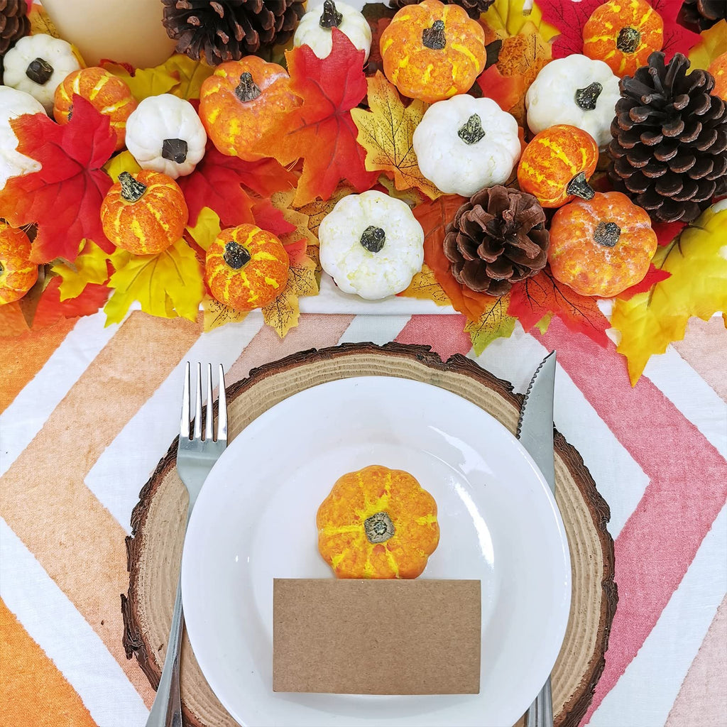Assorted mini pumpkins and pinecones arranged with fall leaves on a table setting with a plate and cutlery.