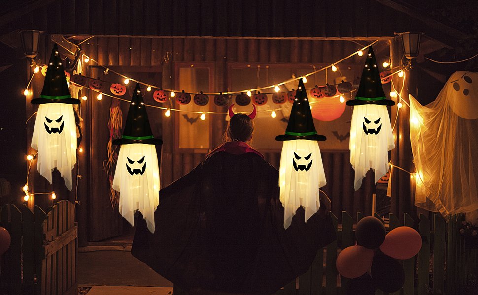 Four glowing ghost decorations with witch hats hang from a string of lights on a porch at night.