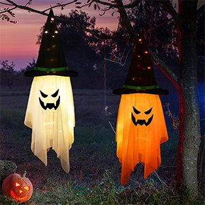 Two glowing witch hat ghost decorations hanging from tree branches, one white and one orange, with a carved pumpkin in the foreground.