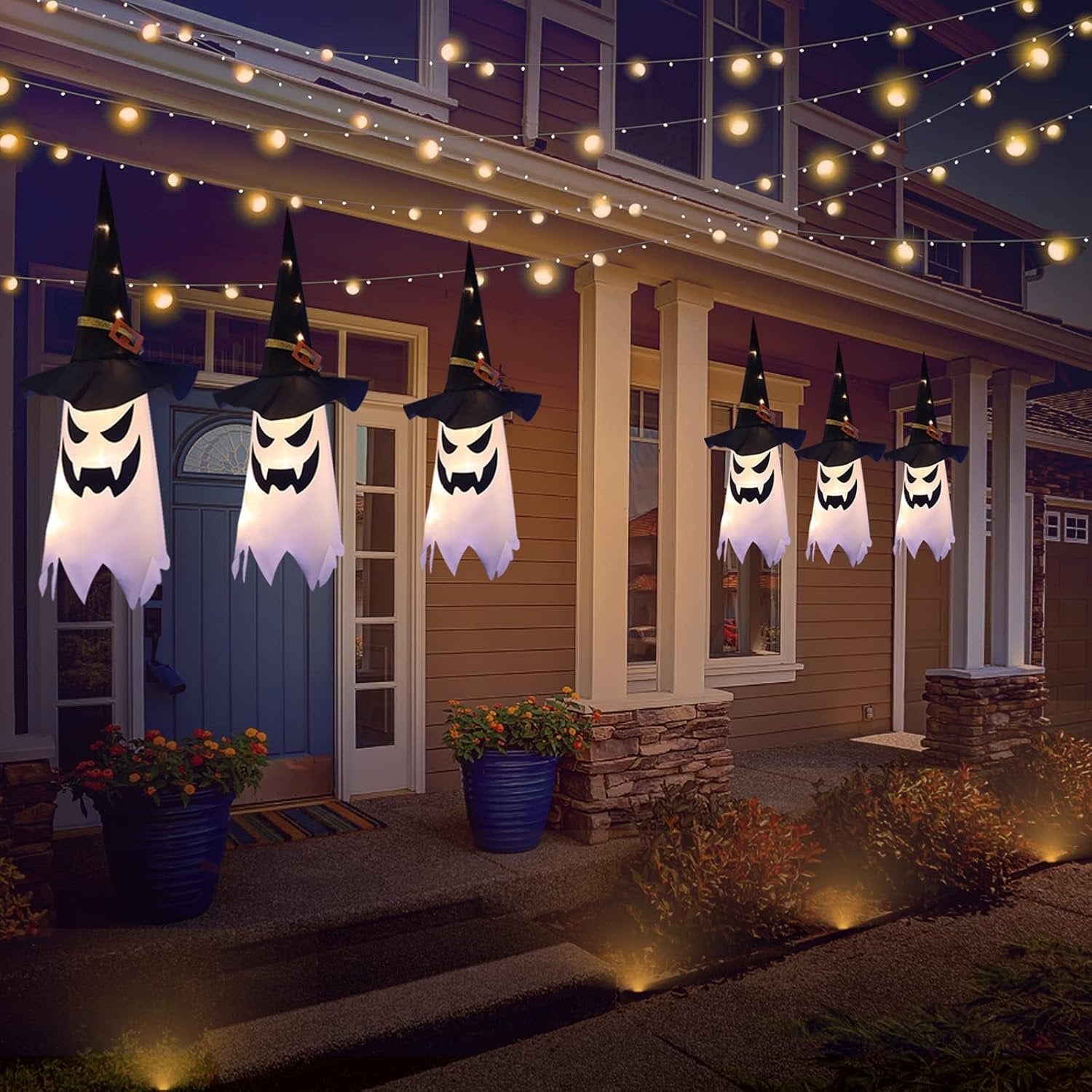Six glowing witch hat ghost lights hanging from a string of lights on a porch at night.