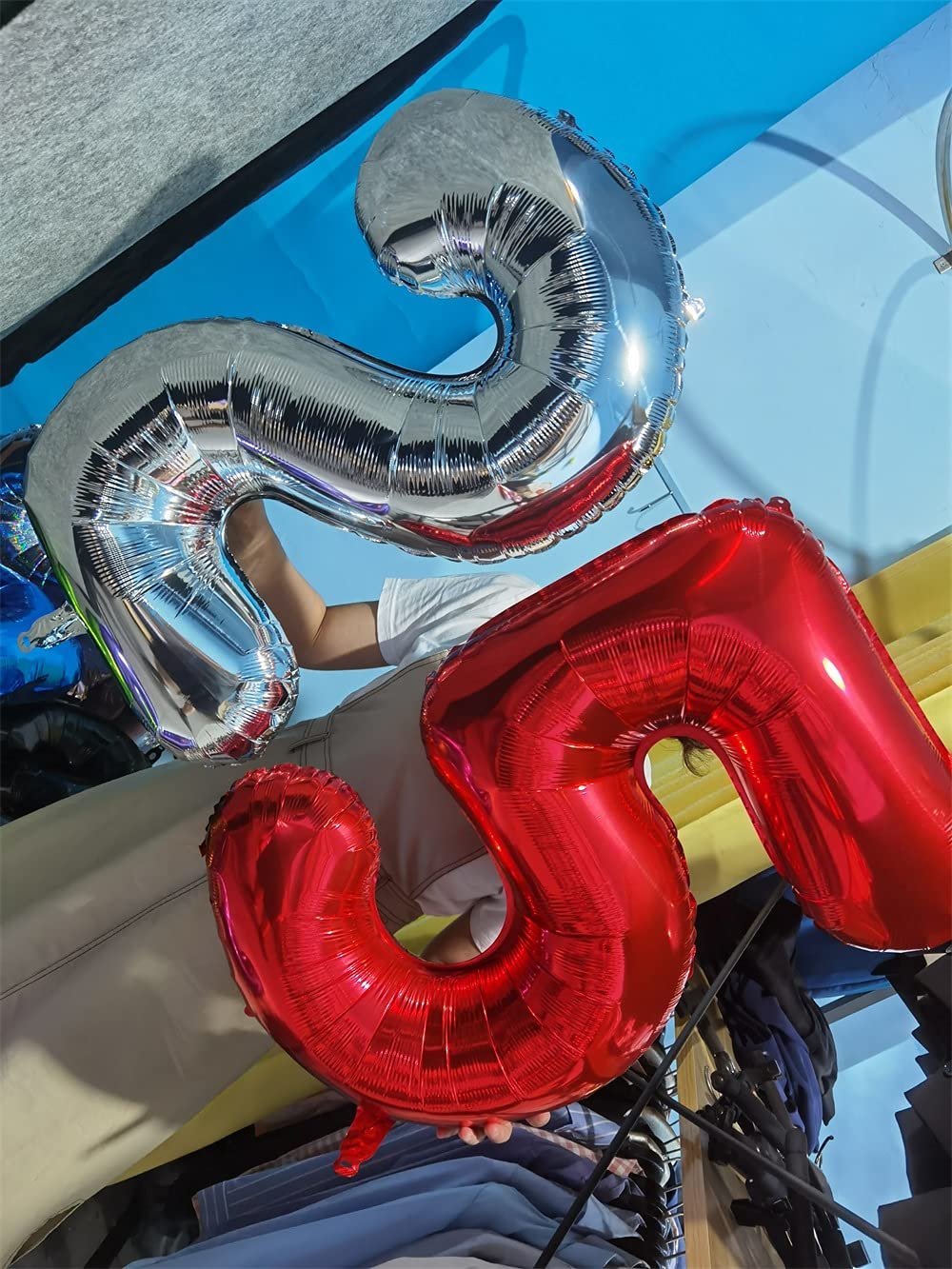 Two large foil number balloons, one red '5' and one silver '9', held by a person wearing a white t-shirt.