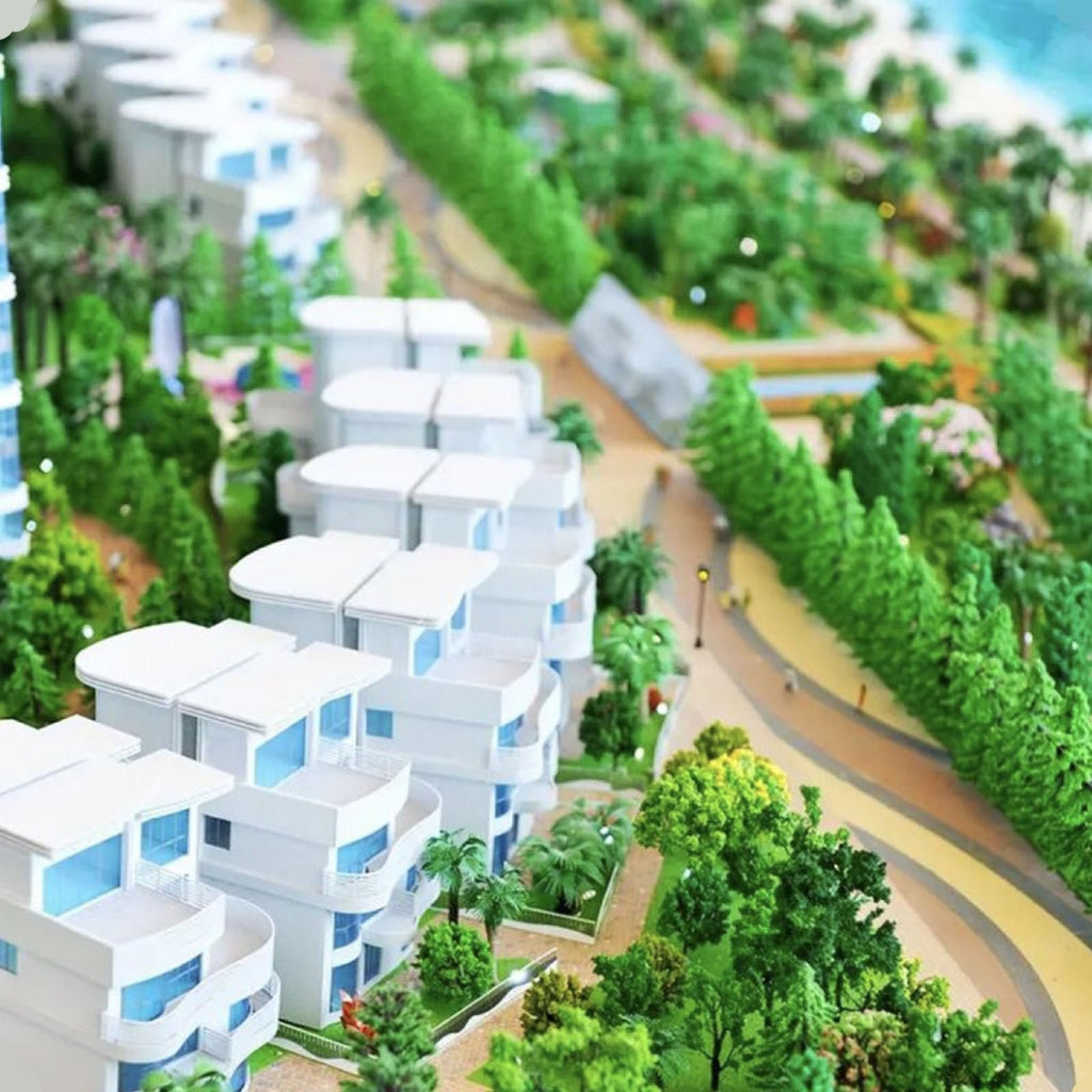Architectural model of a coastal resort with white buildings, lush greenery, and a beach in the background.