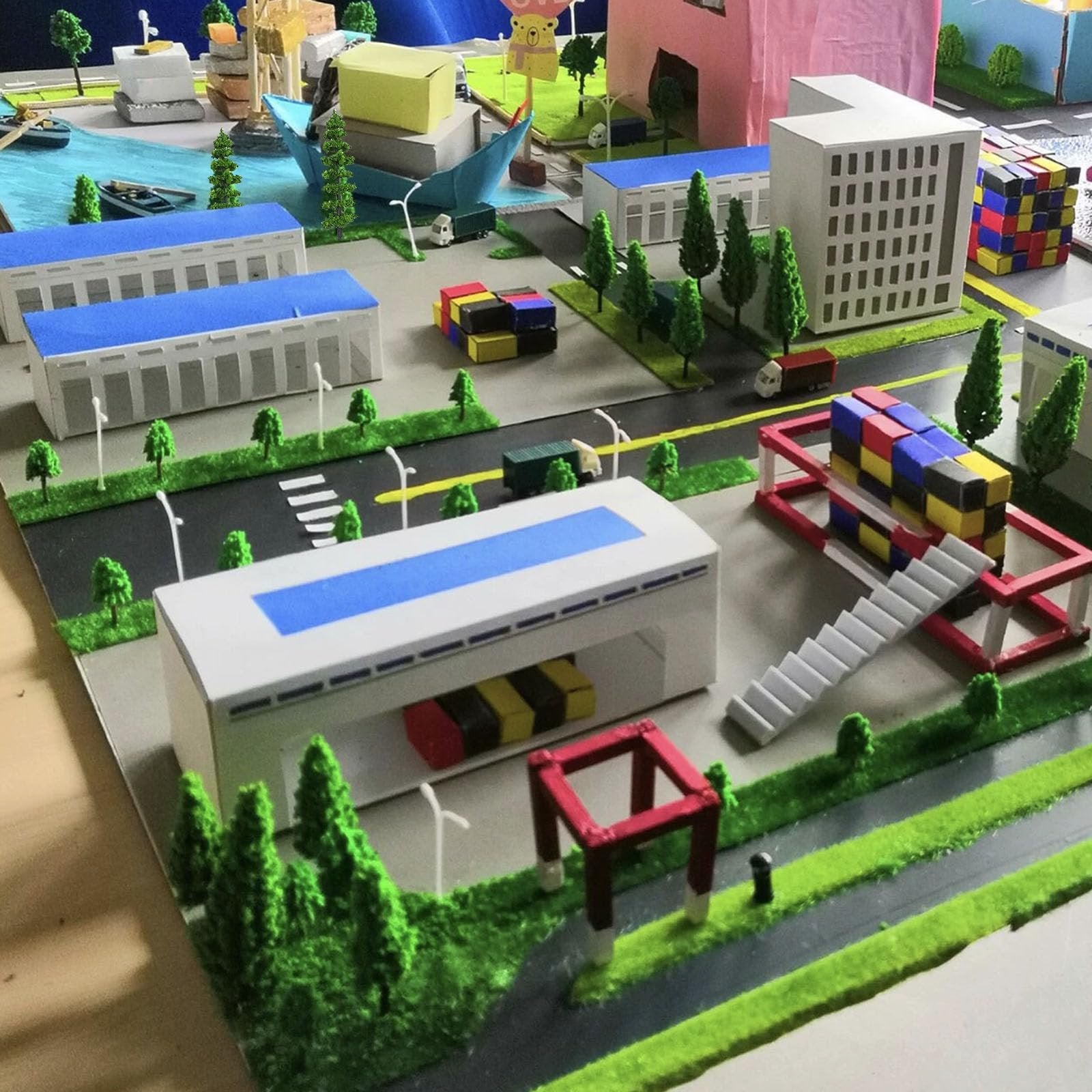 Diorama of a city with buildings, roads, trees, and vehicles, featuring a large white building with blue accents.
