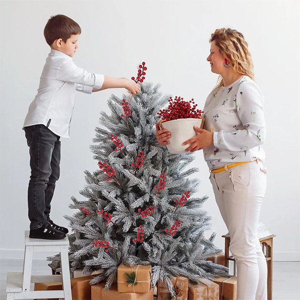 Mother and son decorating a flocked Christmas tree with artificial red berry stems.