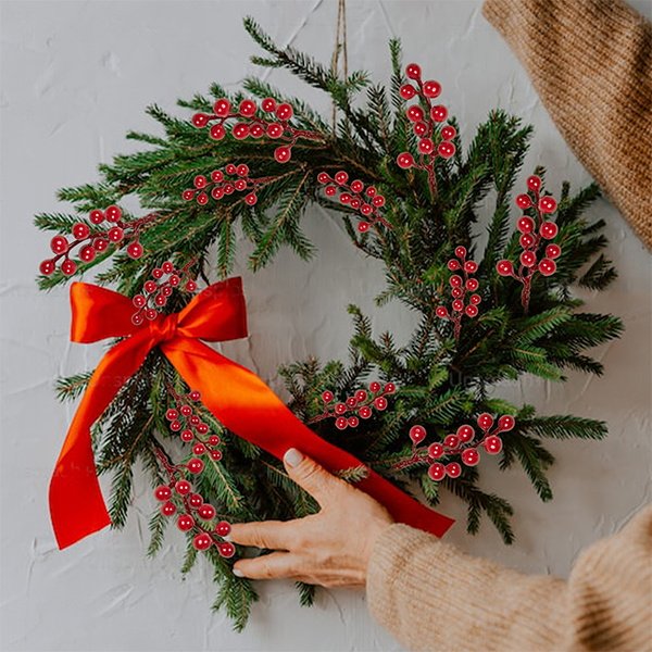 Christmas wreath decorated with artificial red berry stems and a large red bow, hands arranging the wreath.