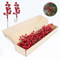Artificial red berry stems with holly berries and pine cone in a circular inset, with stems in an open box