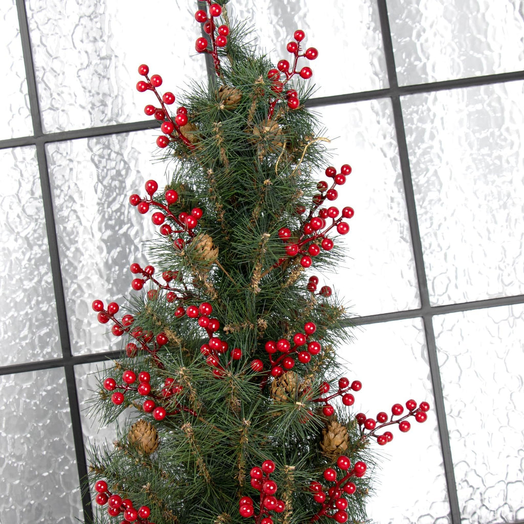 Close-up of a faux pine branch with red berries and pinecones against a frosted window pane.