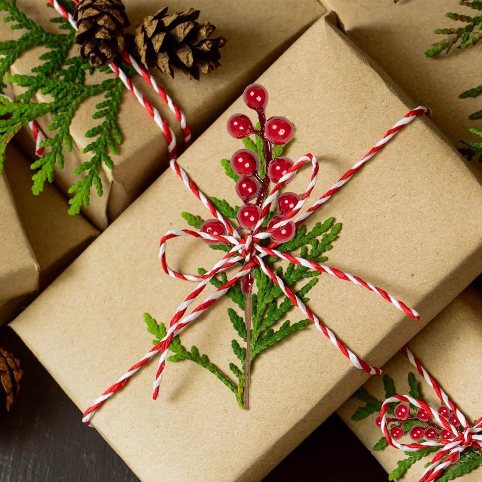 Artificial red berry stems with holly berries and pine cones on wrapped Christmas gifts with red and white twine.