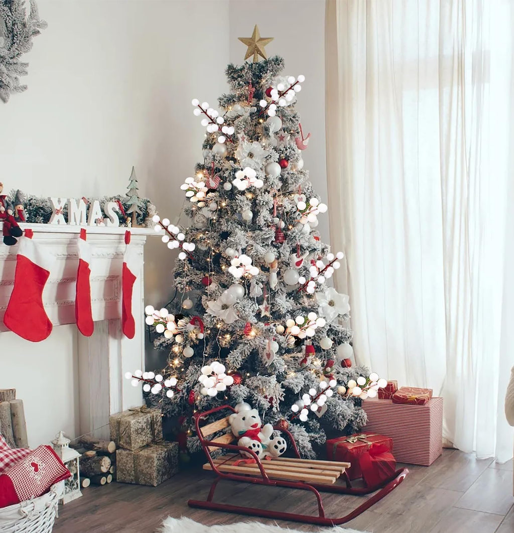 Flocked Christmas tree decorated with white berry stems and ornaments, with a fireplace and stockings to the left.