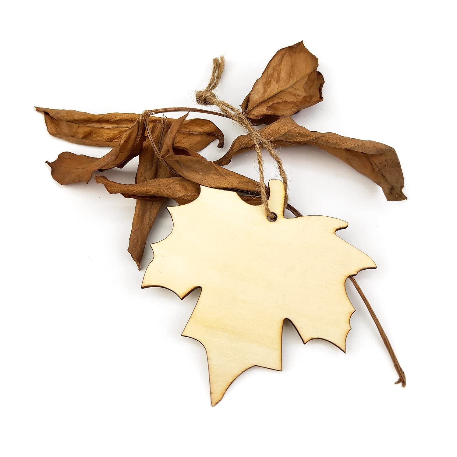 Unfinished wooden maple leaf cutout with twine and dried leaves on a white background