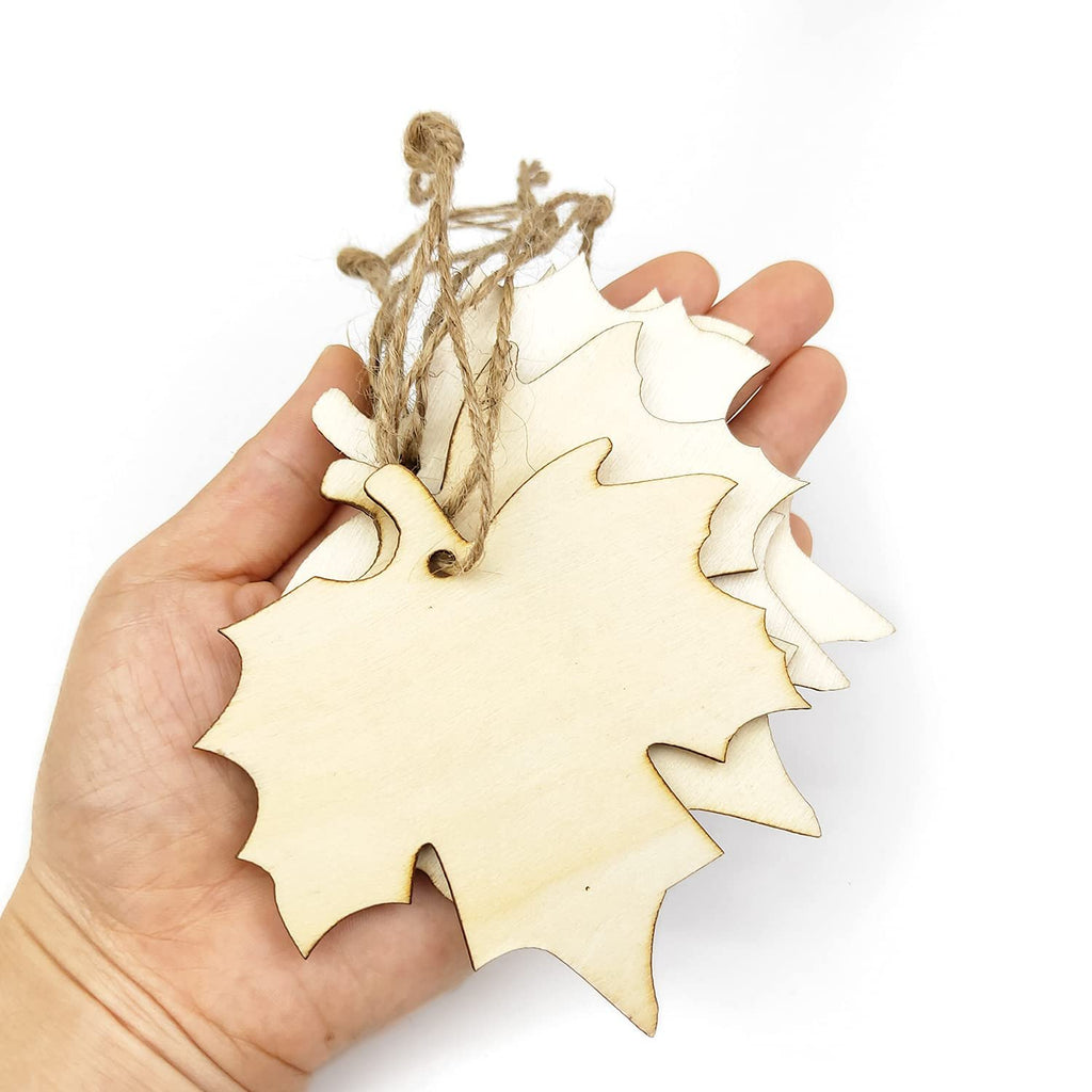 Hand holding a stack of unfinished wooden maple leaf cutouts with twine attached, on a white background.