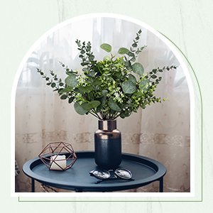 Artificial eucalyptus stems in a dark vase on a side table with a candle holder and glasses.