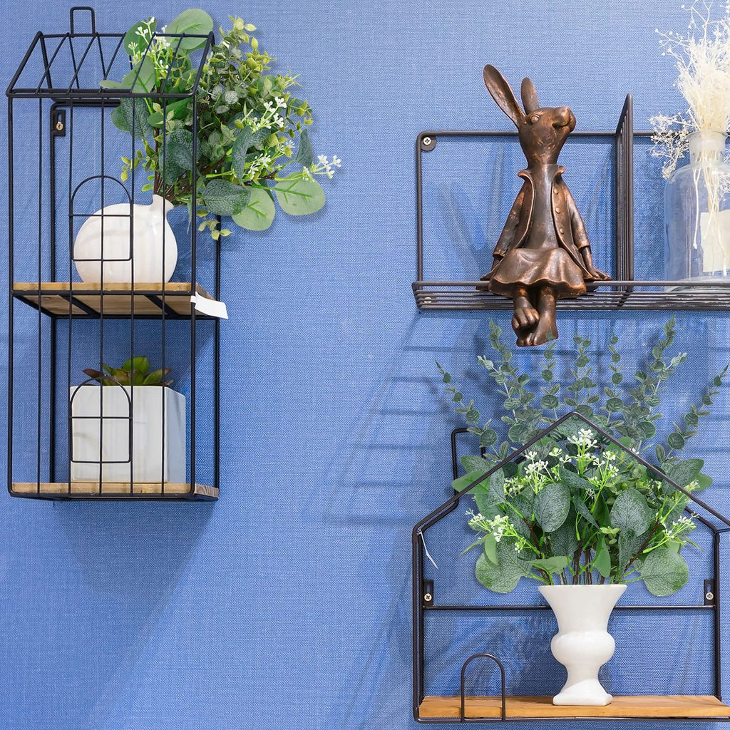 Artificial eucalyptus stems with white flowers in a white vase on a black wall shelf