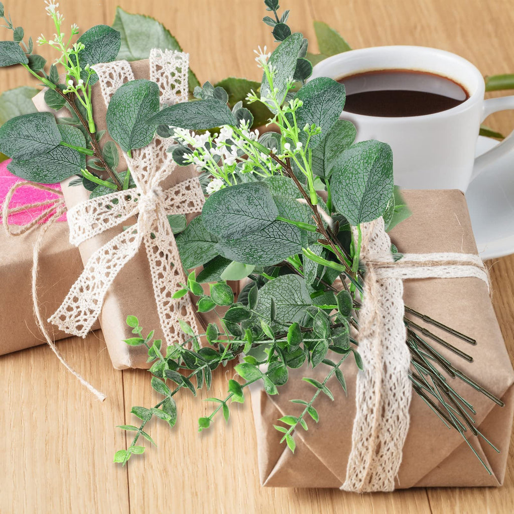 Wrapped gifts adorned with artificial eucalyptus stems and lace ribbons, next to a cup of coffee.