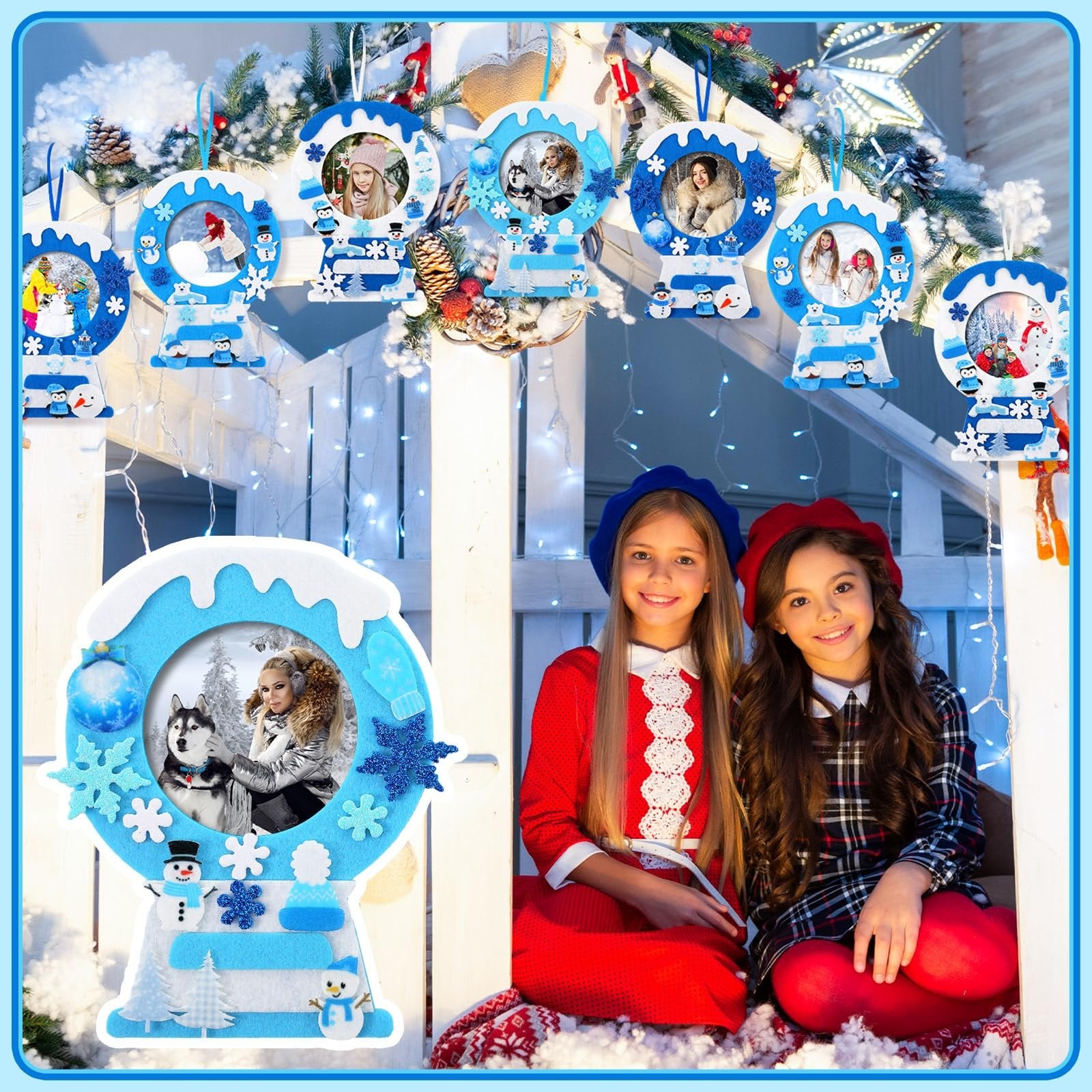 Two girls smiling in front of a display of winter-themed felt picture frame crafts hanging on a railing with fairy lights.