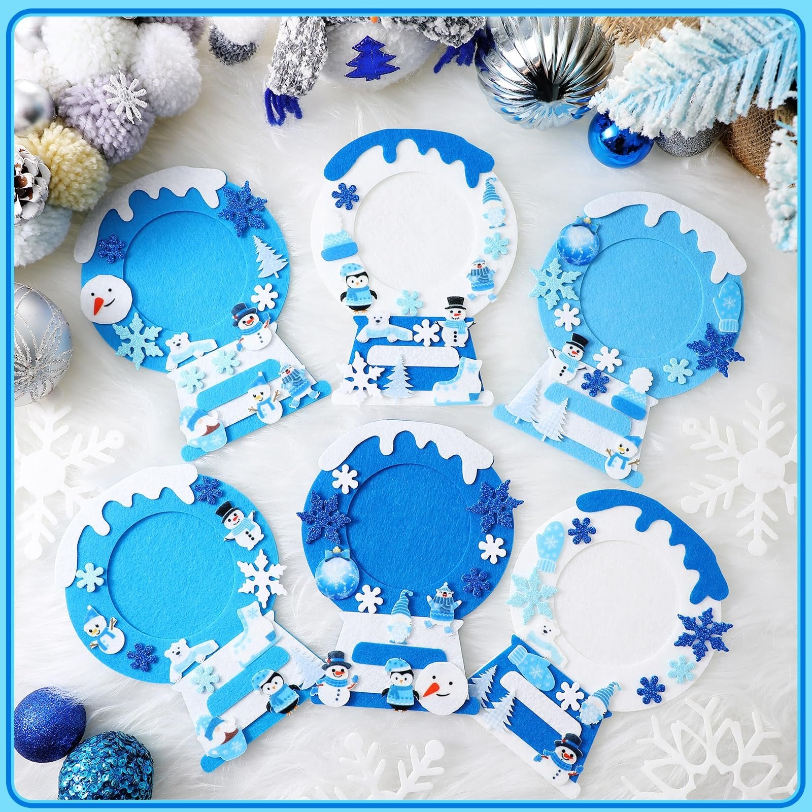 Winter felt picture frame craft kits with snowmen, penguins, and snowflakes, arranged on a white fluffy surface with holiday decorations.