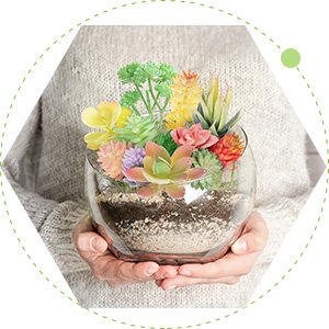 Person holding a clear glass bowl filled with colorful artificial succulents and soil.