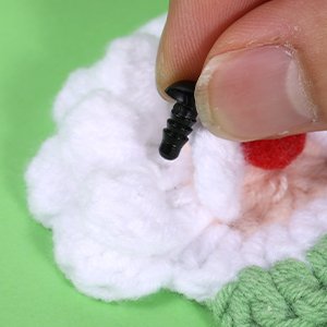 Hand holding a black plastic safety eye screw to attach to a crochet craft project.