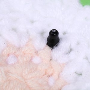 Close-up of a black plastic safety eye inserted into a white and peach crocheted craft project.