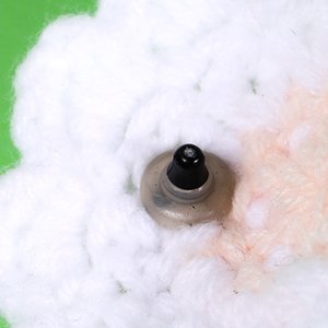 Close-up of a black plastic safety eye with a clear washer attached to white crochet material.