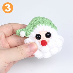Hand holding a small crocheted Santa Claus head with black safety eyes and a green hat