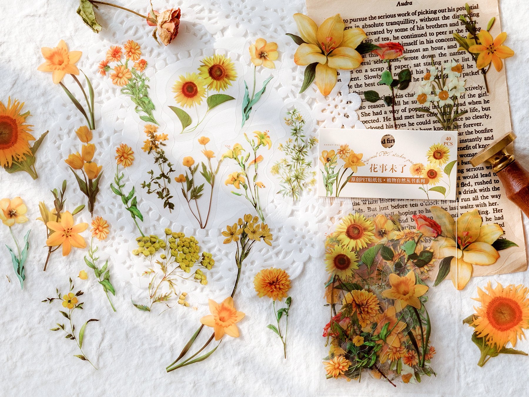 Assorted yellow and orange botanical stickers scattered on a white textured surface with vintage paper and dried flowers.