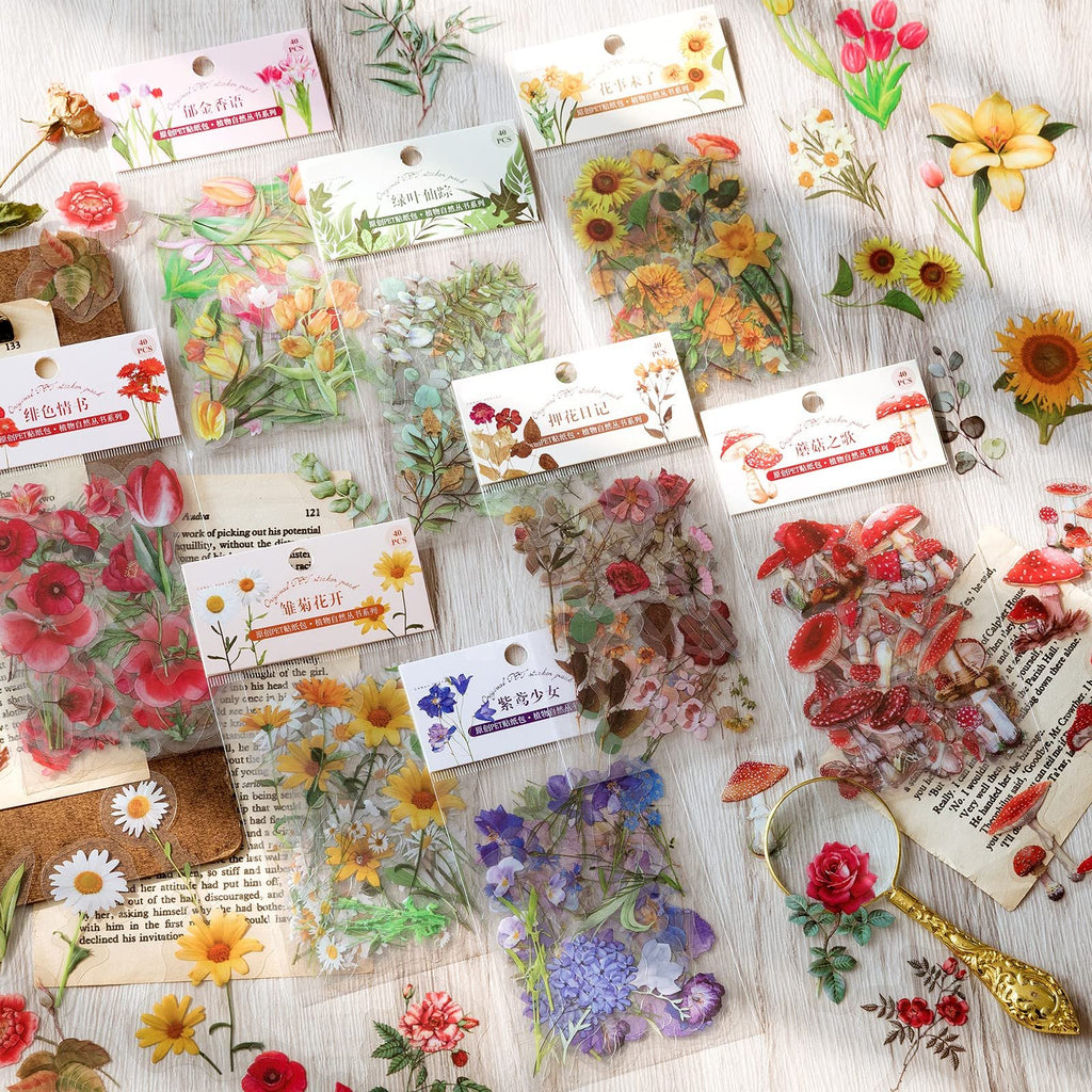 Assortment of clear PET botanical stickers featuring flowers, leaves, and mushrooms, scattered on a wooden surface with vintage book pages.
