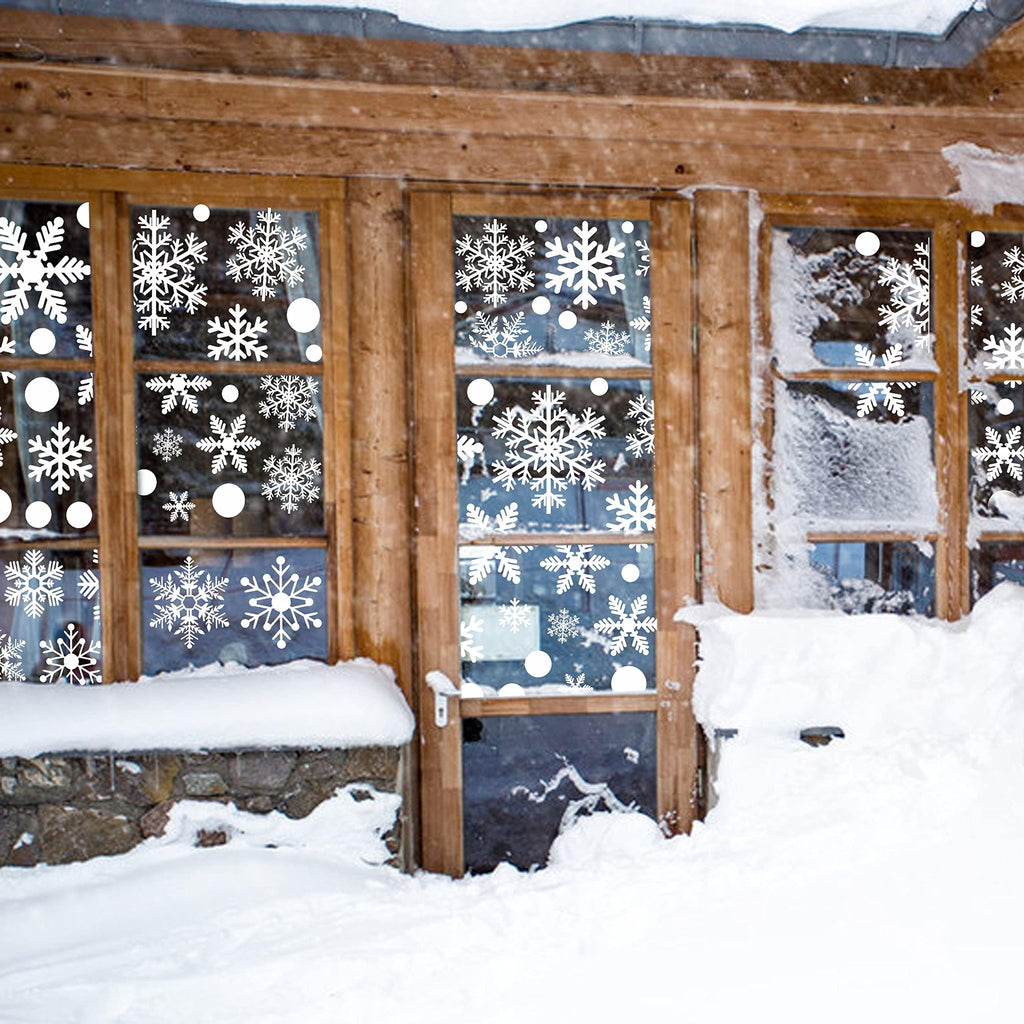 White snowflake and dot window decals applied to wooden-framed windows of a snow-covered cabin.