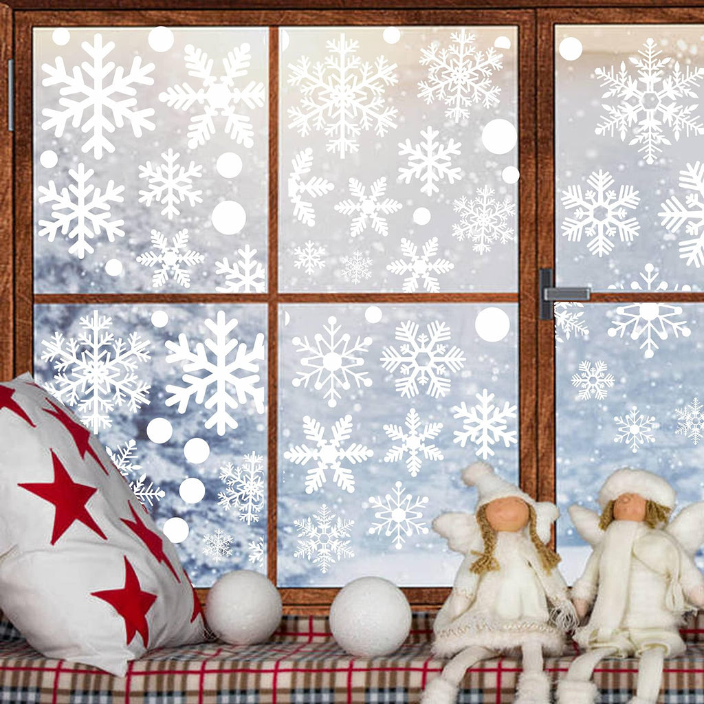 Christmas window decals with snowflakes and circles applied to a window with a snowy scene outside. Two angel figurines sit on the windowsill.