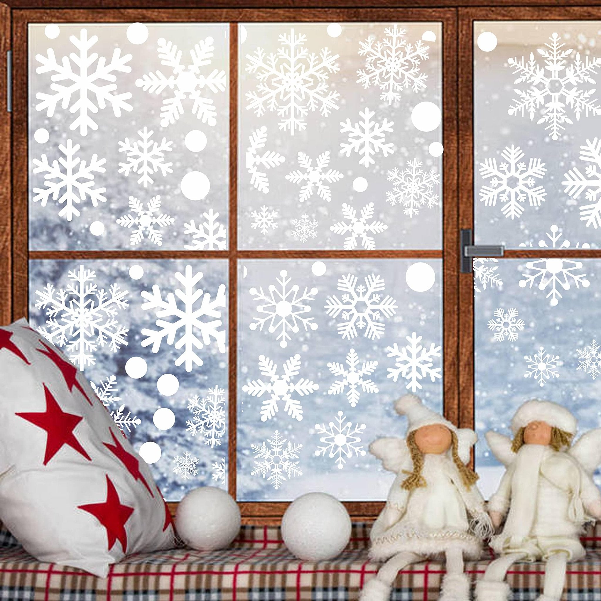 Christmas window decals with snowflakes and circles applied to a window with a snowy scene outside. Two angel figurines sit on the windowsill.