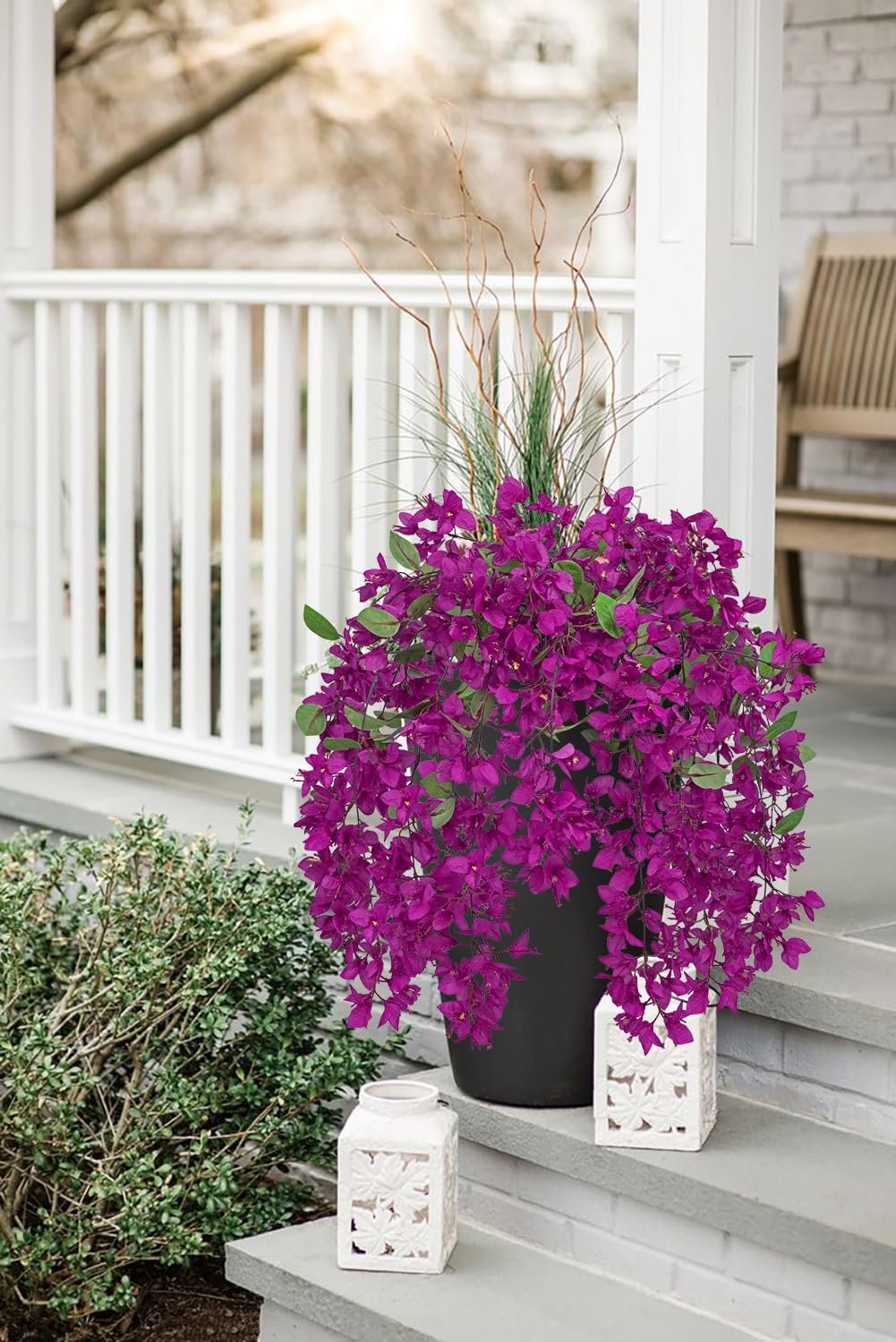 Artificial purple bougainvillea flowers cascading from a black planter on a porch, with decorative lanterns and greenery.