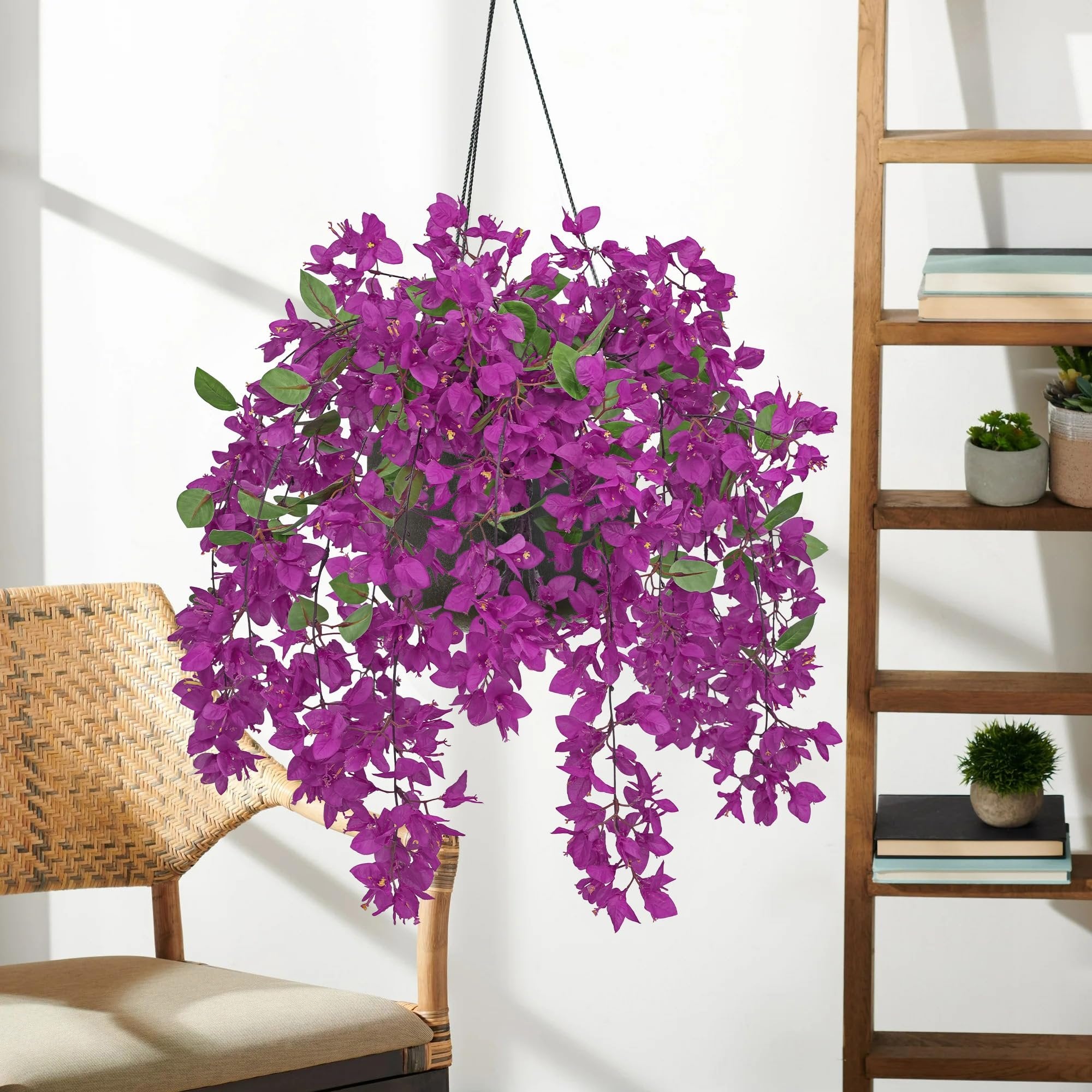 Hanging artificial purple bougainvillea flowers with green leaves, displayed indoors near a chair and bookshelf.