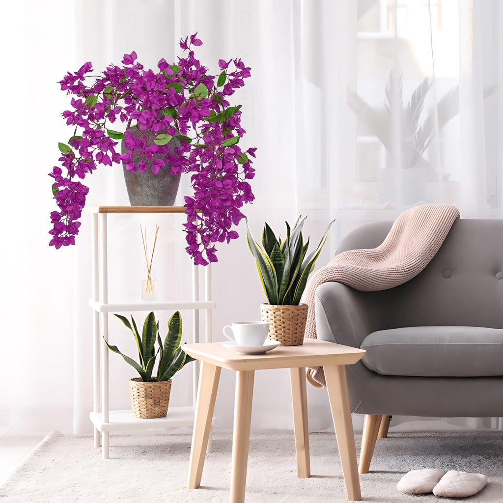 Artificial purple bougainvillea flowers in a grey pot on a shelf, next to a sofa with a pink throw.