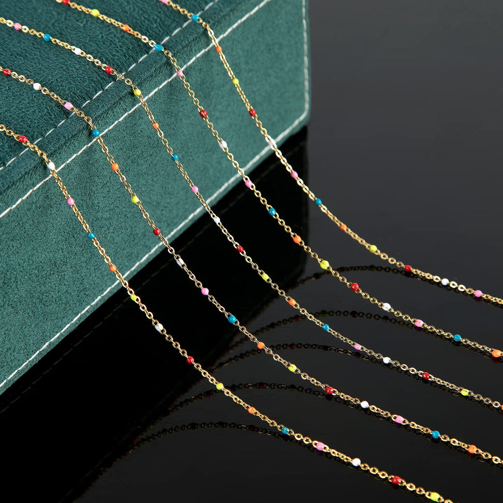 Gold-plated stainless steel beaded jewelry chain with colorful beads, laid out diagonally on a dark surface with a green textured box.