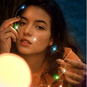 Woman holding color-changing fairy lights with copper wire, lights illuminate her face