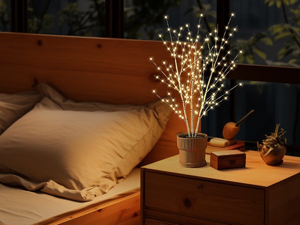 Illuminated birch light tree with 180 LED lights on a bedside table next to a bed.