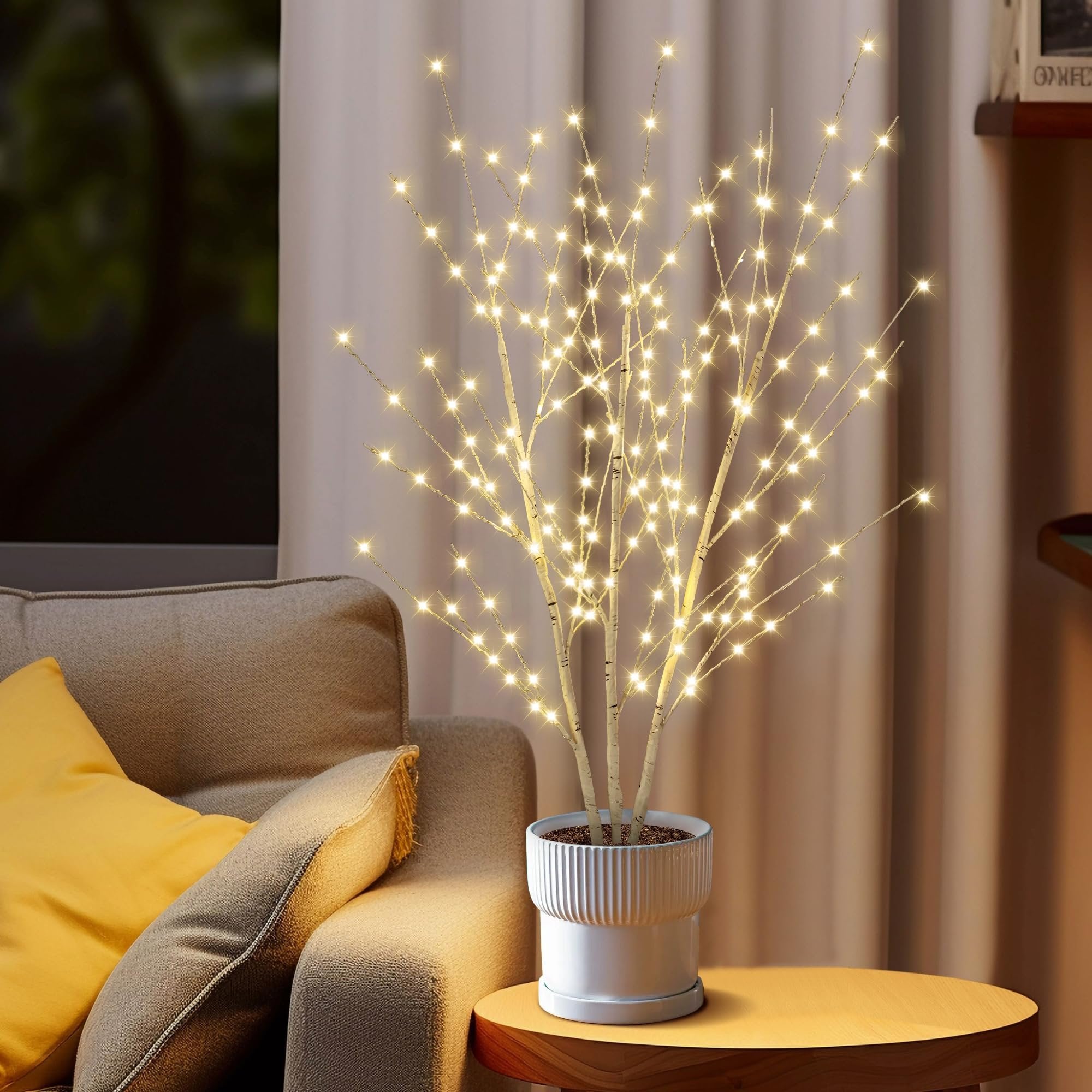 Illuminated birch tree with LED lights in a white pot on a side table next to a sofa.