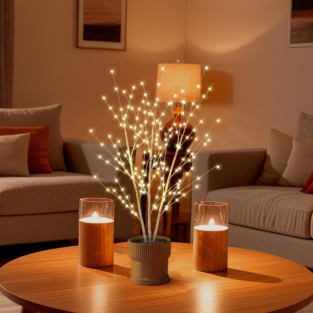Birch light tree with 180 LED lights in a pot on a coffee table with two candle lanterns, set in a living room.