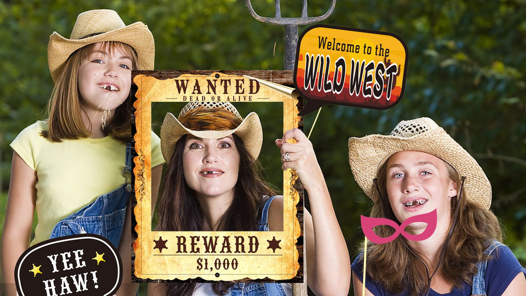 Three girls in cowboy hats posing with western-themed photo booth props including a wanted poster frame and a welcome sign.