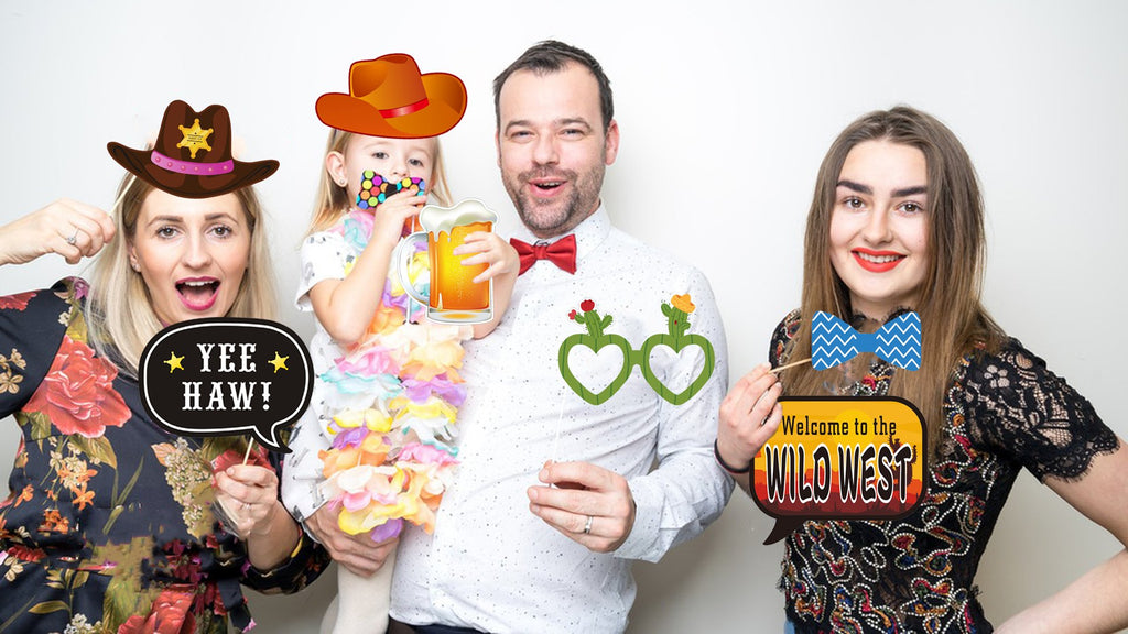 Family posing with western-themed photo booth props including hats, a beer mug, and a 'Wild West' sign.