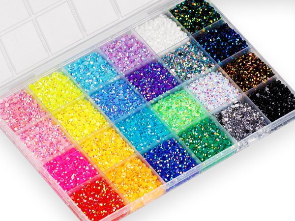 Clear plastic organizer box filled with colorful flatback rhinestones in various sizes and shades, including pink, yellow, blue, green, purple, white, black, and iridescent.