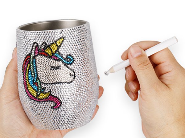 Hands decorating a cup with rhinestones using a tool, featuring a unicorn design.