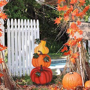 Stacked hand-painted pumpkins garden stake with fall leaves and a white picket fence.