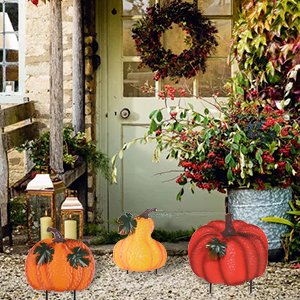 Three stacked hand-painted pumpkin garden stakes with wind-moving leaves displayed outdoors near a doorway.