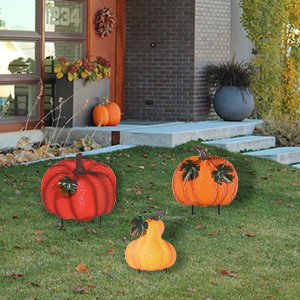Three stacked metal garden stakes shaped like pumpkins and gourds, decorated for fall, placed on a lawn in front of a house.