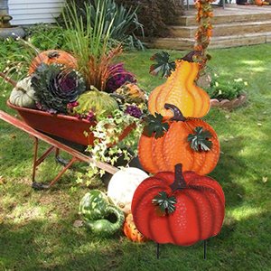 Stacked hand-painted pumpkins and gourds in a wheelbarrow and on the lawn, decorated for fall outdoor display.