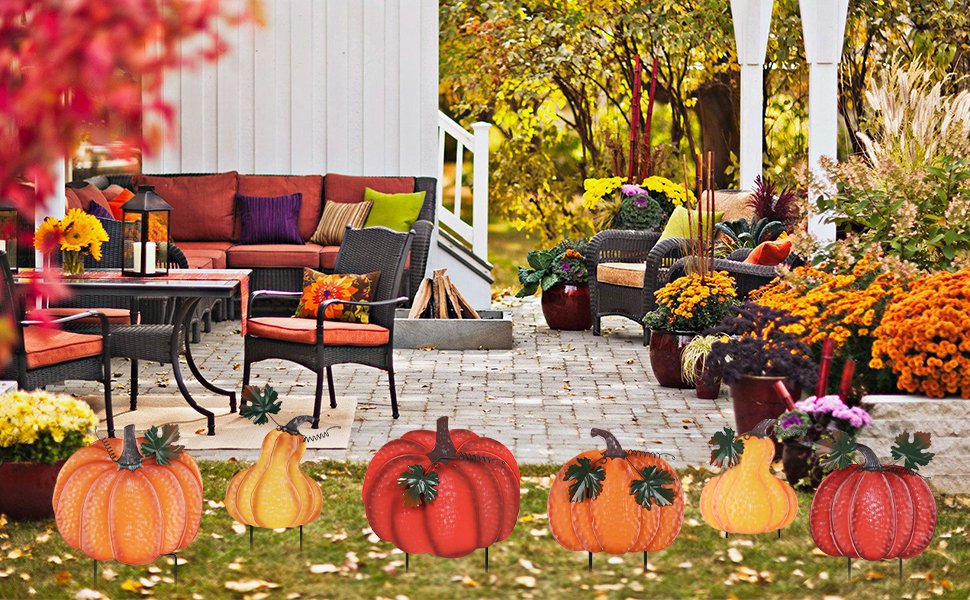 Fall outdoor decor featuring stacked hand-painted pumpkins and gourds on garden stakes in front of a patio seating area.