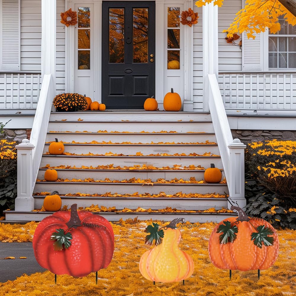 Three stacked metal pumpkins with wind-moving leaves as outdoor fall decor on a lawn in front of a house porch.