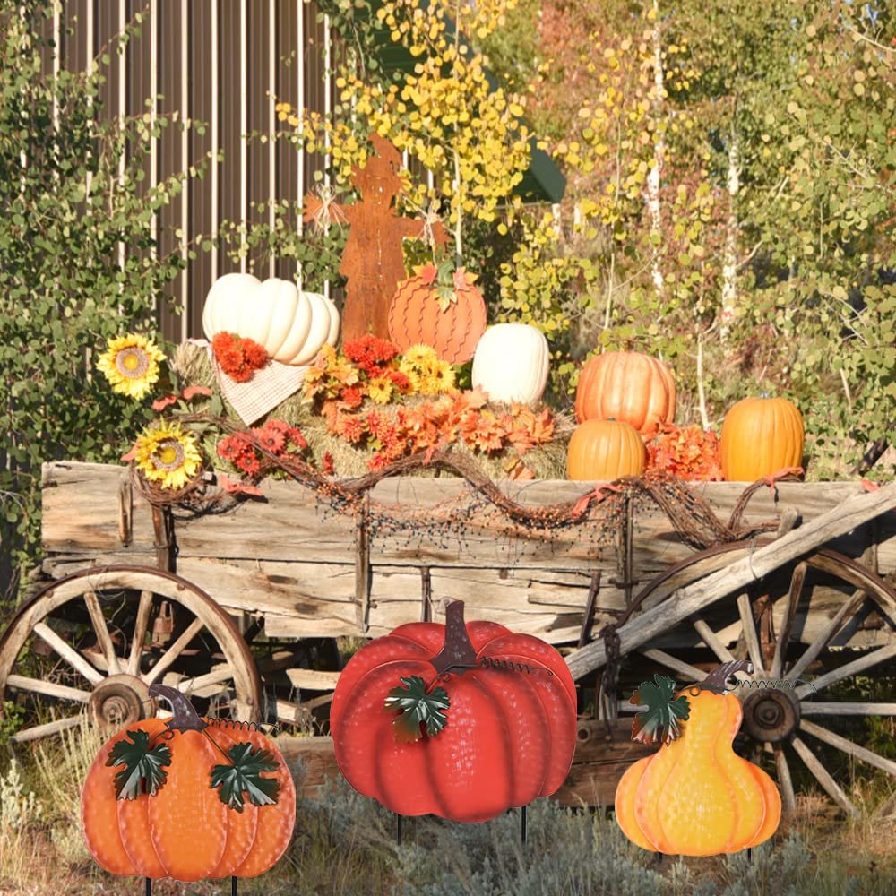 Three stacked hand-painted metal pumpkins with wind-moving leaves garden stakes in front of a rustic wagon display.
